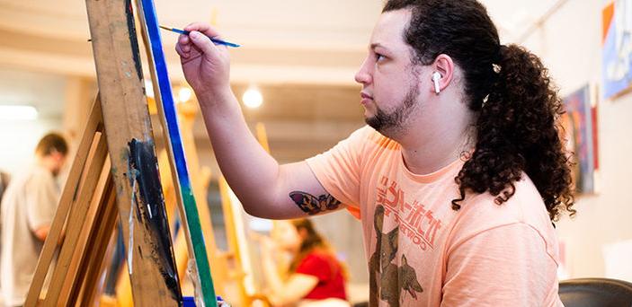a BSU student painting at an easel with other students painting in the background