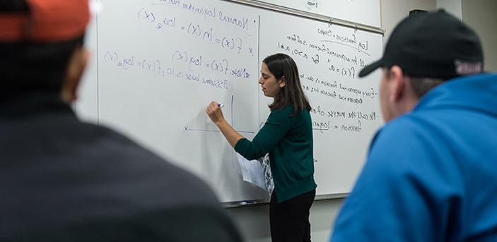 BSU Math professor Rachel Stahl writes on a white board under the words "Natural Logarithm function" while students look on